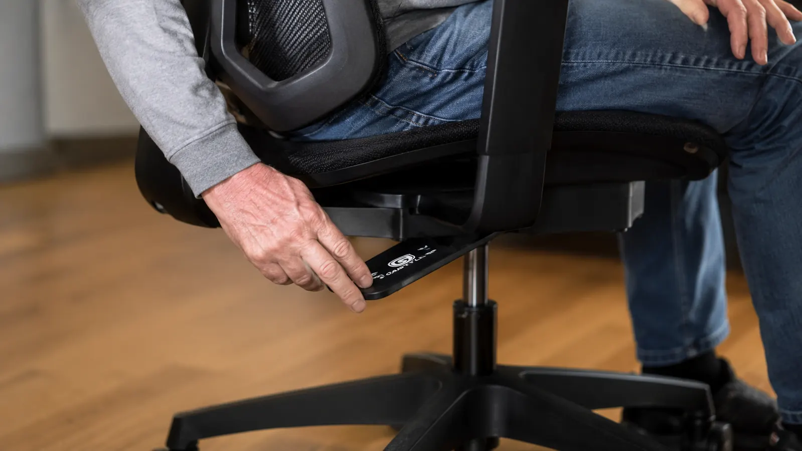 Close-up of a hand adjusting the seat height lever underneath an ergonomic office chair